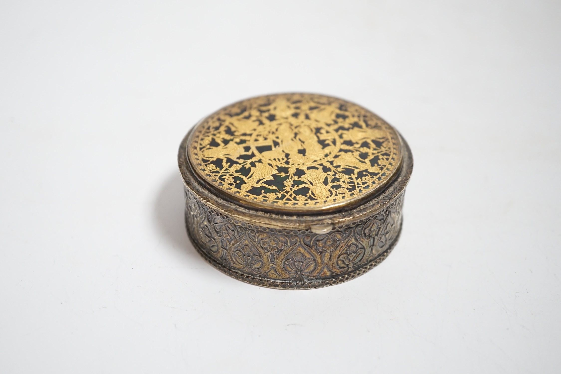 An Indian? embossed white metal circular box, with gilt and enamelled hinged cover decorated with Indian dancers, diameter 73mm.